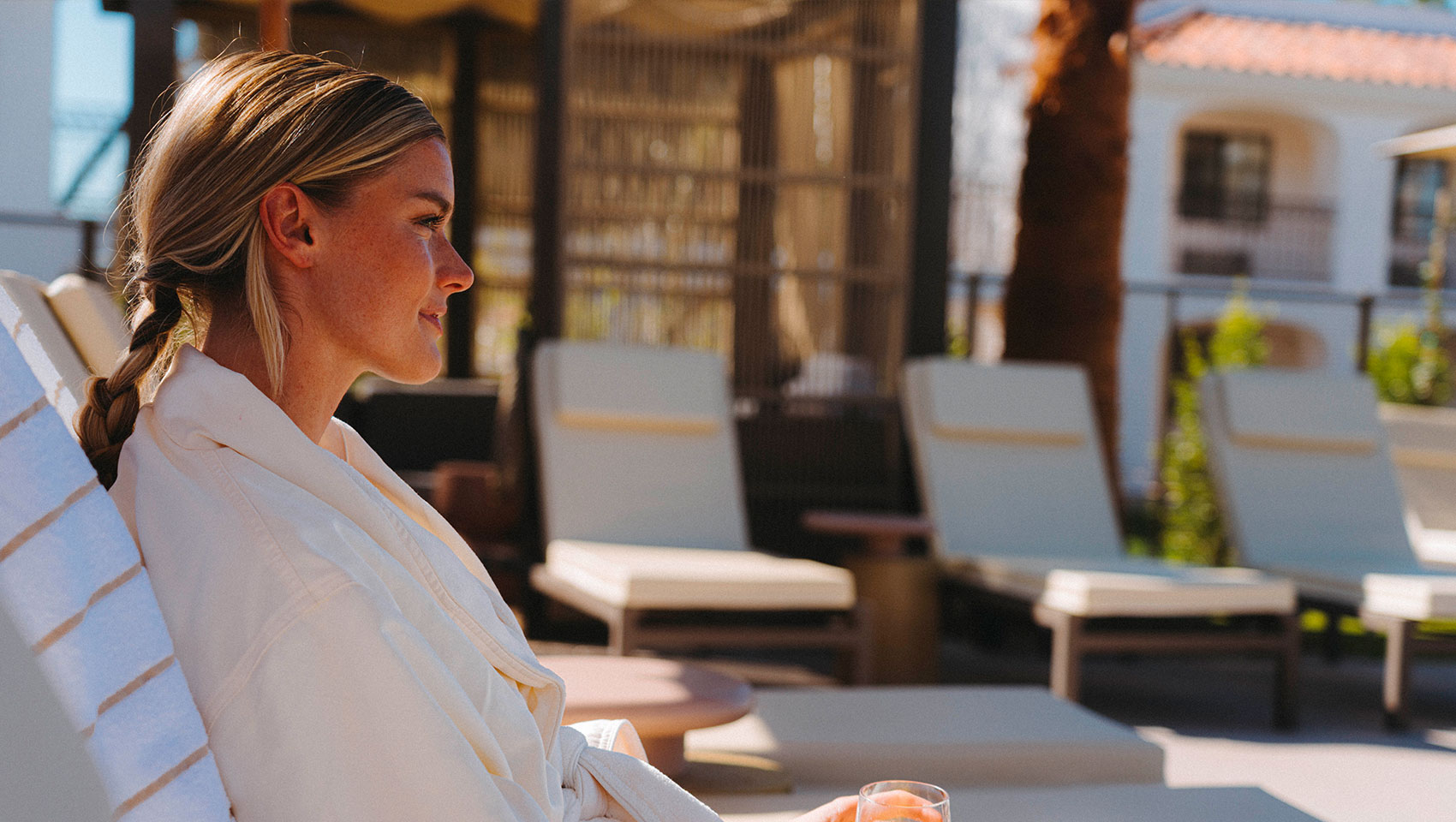 woman in spa robe lounging outside with a drink