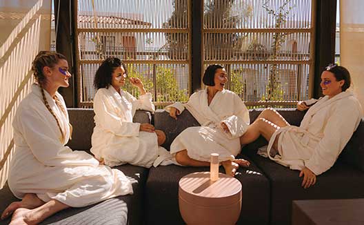 4 women in robes sit in outdoor structure chatting and wearing eye masks at Kimpton Miralina Resort