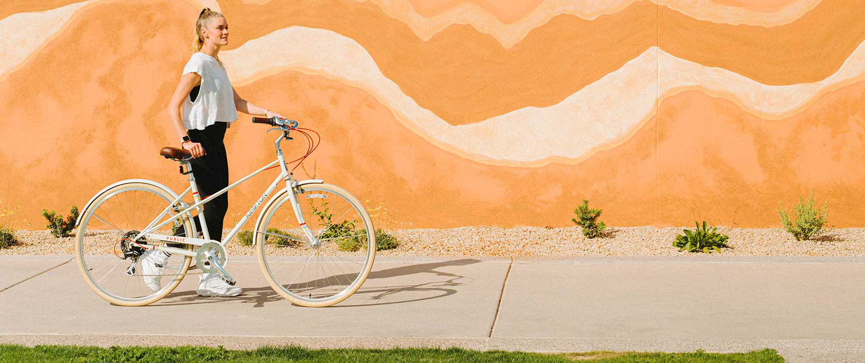 Woman walks with bicycle in front of art wall